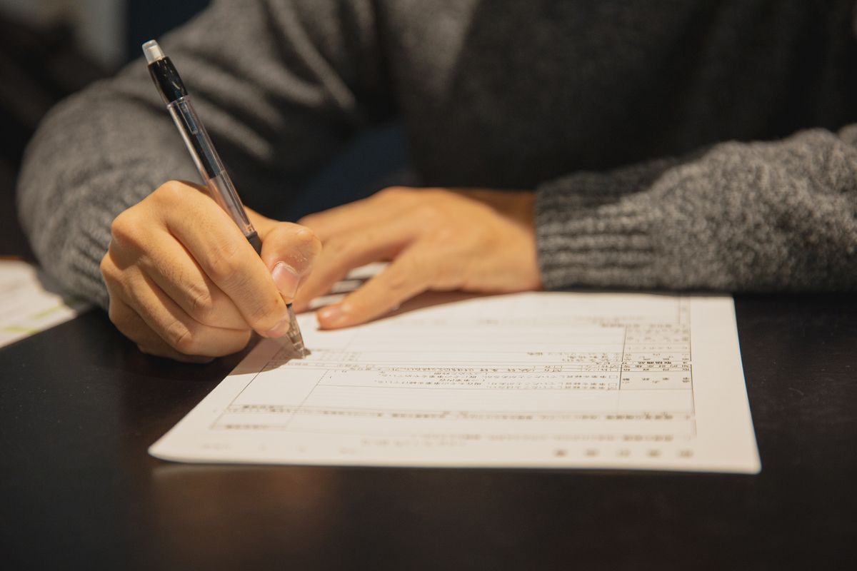 A hand filling in a printed form with a pen at a wooden table.