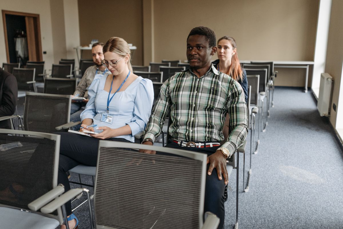 A small group of adults seated in a plain training room, one taking notes.