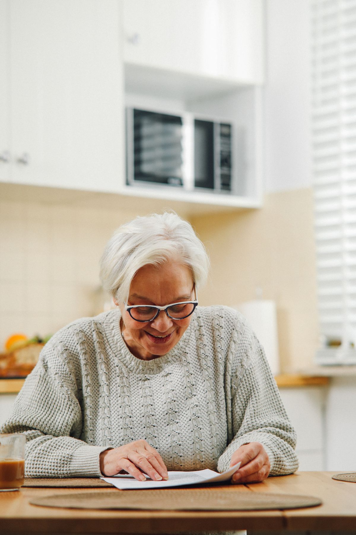 An older woman in glasses reading printed course material at her kitchen table.